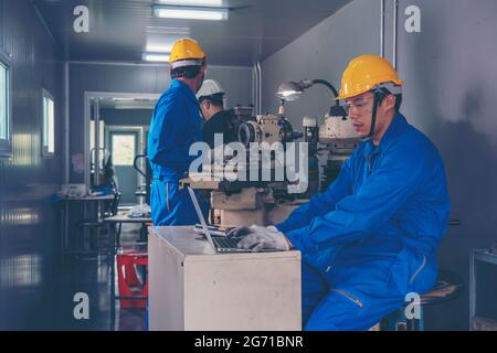 Machinist indossando un guanto di sicurezza per la protezione degli occhi mentre si utilizza una mola da tavolo per la finitura del metallo. Uomo che lavora la rettificatrice per tornio me Foto Stock