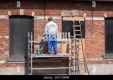 Sint Gillis WAAS, Belgio, 21 aprile 2021, il pittore si erge su un ponteggio e ispeziona un vecchio muro di pietra Foto Stock