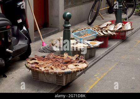 Stile di vita locale della gente macanese pesce sole essiccato per conserve alimentari su cesto di vimini di bambù all'aperto sul sentiero accanto alla strada a Macao Foto Stock