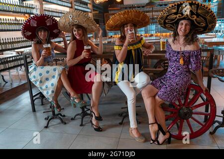 Gruppo di donne mature sta bevendo birra in un pub che indossa sombreros messicani Foto Stock