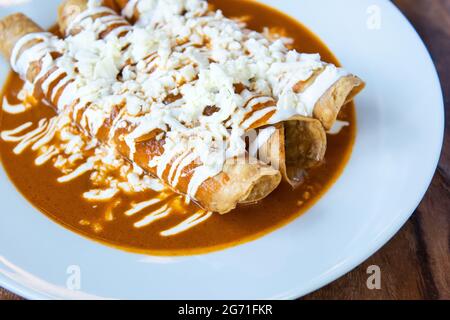 Primo piano di deliziosi tacos annegati in salsa rossa su un piatto bianco Foto Stock