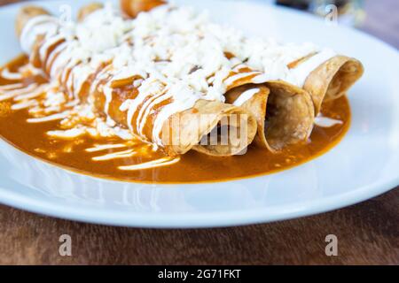 Primo piano di deliziosi tacos annegati in salsa rossa su un piatto bianco Foto Stock