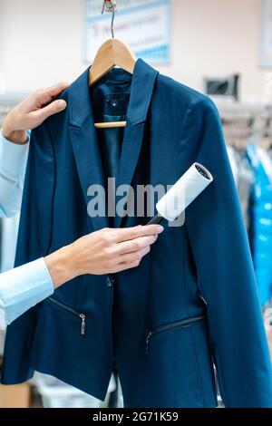 Una donna dedicata nel negozio di pulizia a secco utilizza un rullo di pelucchi per pulire una camicia Foto Stock