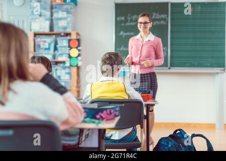 Studenti in classe desiderosi di rispondere a una domanda al loro insegnante, tutti alzando la mano Foto Stock