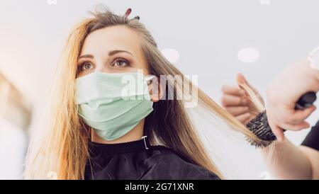 Donna che visita il parrucchiere e ottenere un nuovo stile di indossare maschera facciale Foto Stock