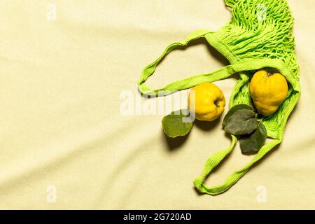 Mele cotogne con foglie in sacchetto di maglia verde su fondo di lino naturale color pastello rugoso. I frutti organici hanno difetti naturali, macchie, graffi Foto Stock