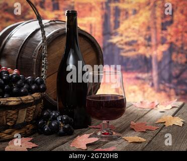 Bicchiere di vino rosso e uva fresca all'aperto su un rustico tavolo in legno con sfondo autunnale Foto Stock