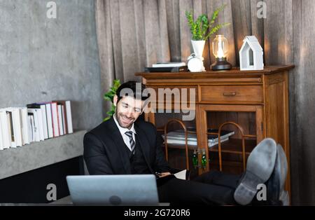 uomo d'affari riuscito a rilassarsi o dormire dopo il lavoro finito ha messo i piedi sulla scrivania. Dipendente del CEO che guarda il notebook dello schermo seduto con le gambe sulla ta Foto Stock