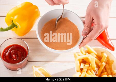Vista dall'alto su una mano che mescola la salsa andalouse con un cucchiaio Foto Stock