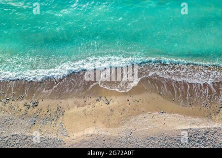 Onde di mare che si infrangono sulla spiaggia selvaggia con sabbia e ciottoli, punto di vista drone direttamente dall'alto Foto Stock