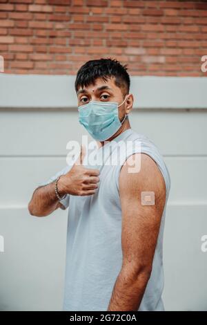Uomo argentino in una maschera che mostra il cerotto sul braccio dopo essere stato vaccinato per COVID-19 Foto Stock