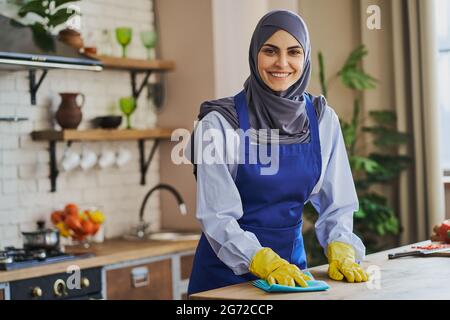 Ritratto di una casalinga araba che pulisce un tavolo in cucina Foto Stock