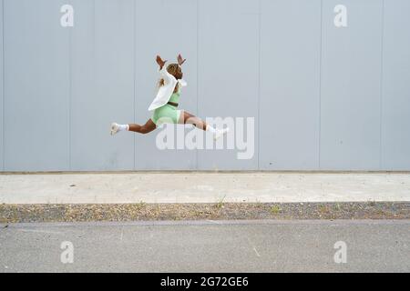 Ritratto a lunghezza intera di una donna afro-americana che salta con gambe spalmato e braccia estese. Donna in abbigliamento sportivo e giacca bianca con trecce gialle Foto Stock