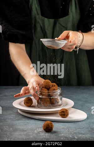 Una donna cospargete le palle di cioccolato con polvere di cacao. Concetto di cucina sana Foto Stock