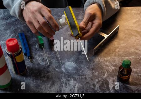 Versare l'olio su una pietra. il knifemaker è in possesso di olio e di un affilatore. Le mani del padrone. Vista frontale. Foto Stock