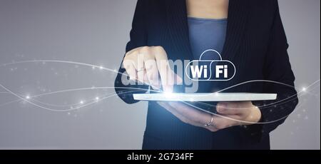 Tablet bianco a mano di una donna d'affari con ologramma digitale Wi-Fi su sfondo grigio. Internet gratuito con tecnologia di segnale di rete WiFi Foto Stock