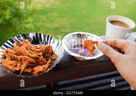 Femmina che mangia gustosa pakoda di cipolla o pyaz KE pakode, bhajiya. Tè indiano pakistano snack frittelle di cipolla immersa in salsa di ketchup di pomodoro con tazza o Foto Stock