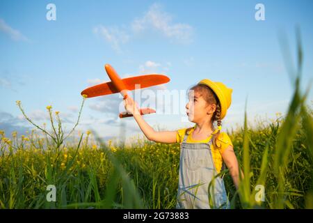 Ragazza in un cappello giallo panama lancia un aereo giocattolo nel campo. Estate, infanzia, sogni e incuria. Tour aereo da un'agenzia di viaggi su un t Foto Stock