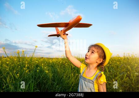 Ragazza in un cappello giallo panama lancia un aereo giocattolo nel campo. Estate, infanzia, sogni e incuria. Tour aereo da un'agenzia di viaggi su un t Foto Stock
