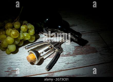 L'autunno è il momento della vinificazione. Composizione con una bottiglia di vino, un mazzo di uve bianche e un cavatappi su fondo ligneo. Foto Stock