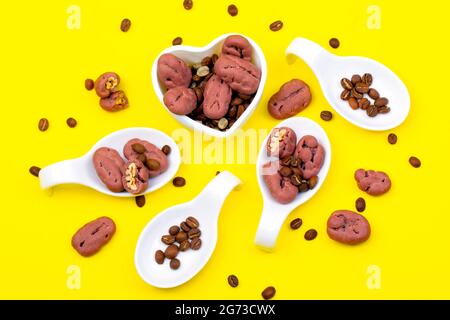 Esempio creativo di mockup di miscela di noci e chicchi di caffè in una ciotola di ceramica bianca. Fondo giallo isolato a giacitura piatta. Foto Stock