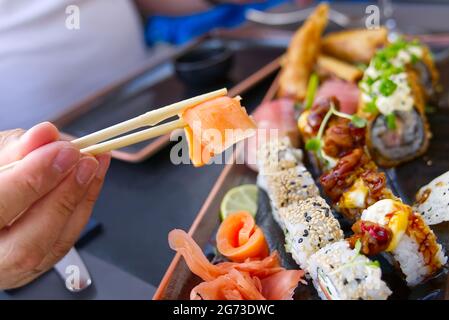 uomo che mangia sashimi di salmone in ristorante giapponese. Uomo che tiene i chopsticks che mangia sashimi di salmone fresco Foto Stock