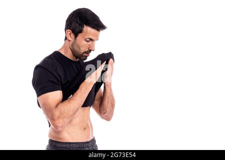 L'uomo europeo, caucasico, un atleta, strofina il sudore dalla fronte con una T-shirt. Dopo un duro allenamento. Stress e fatica. Su sfondo bianco. Foto Stock