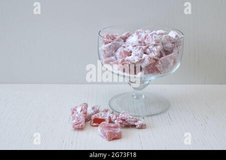 Pezzi di zucca essiccati in zucchero in polvere in una ciotola di vetro e su un tavolo di legno. Prelibatezze Foto Stock