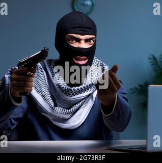 Il terrorista ladro con la pistola lavorando al computer Foto Stock