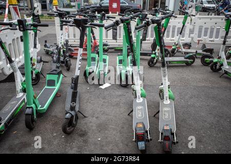 Fila di e-scooters di varie aziende, con Eco friendly mobilità concetto di condivisione scooter elettrico, parco sul marciapiede di fronte a stile europeo. Foto Stock