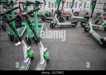 Fila di e-scooters di varie aziende, con Eco friendly mobilità concetto di condivisione scooter elettrico, parco sul marciapiede di fronte a stile europeo. Foto Stock