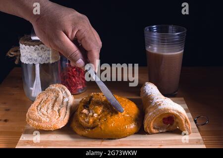 Una mano maschile che taglia un pane dolce con un coltello su un pannello di legno Foto Stock