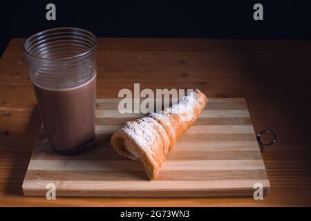 Una gustosa caramella a forma di cono e un bicchiere di cioccolato su una tavola di legno sul tavolo Foto Stock