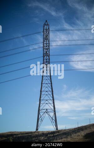 Torre di trasmissione elettrica con struttura a traliccio, collegata a linee elettriche che corrono in parallelo attraverso il cielo azzurro con alcune nuvole in autunno Foto Stock