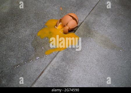 Uovo smasched su pavimento grigio mattonella con cracked e rotto guscio, tuorlo d'uovo e albume spruzzi Foto Stock