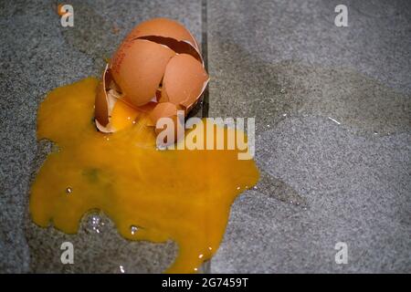 Uovo smasched su pavimento grigio mattonella con cracked e rotto guscio, tuorlo d'uovo e albume spruzzi Foto Stock