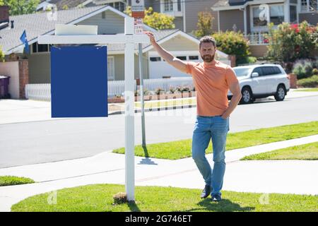 Agente immobiliare uomo d'affari con casa in vendita segno in piedi vicino immobile residenziale fuori. Foto Stock