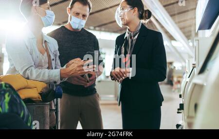 Coppia che mostra il telefono cellulare al personale dell'aeroporto durante la pandemia. Famiglia turistica che si prende l'aiuto di un assistente di terra all'aeroporto in pandemia. Foto Stock