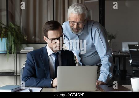 Professionista anziano che dà aiuto, consiglio ai giovani collaboratori Foto Stock