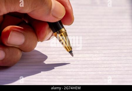 Scrittura con la mano sinistra con una penna d'oro, a fuoco basso su carta rivestita bianca Foto Stock