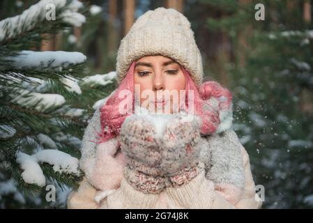 Bella ragazza con i capelli rosa soffia la neve nelle mani Foto Stock