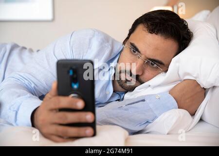 uomo arabo di media età a letto con il telefono Foto Stock