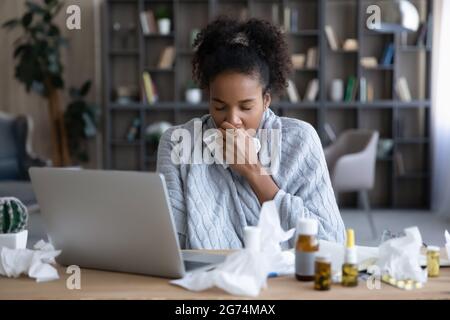 Donna d'affari afroamericana malsana avvolta in plaid che soffia il naso che corre Foto Stock