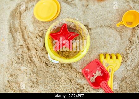 Vista dall'alto, disposizione piatta di giocattoli sparsi in plastica sulla spiaggia sullo sfondo di sabbia, vacanza estiva in famiglia, sfondo con spazio vuoto per il testo Foto Stock