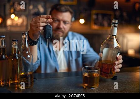 Uomo ubriaco con la chiave dell'auto seduta al bancone del bar Foto Stock