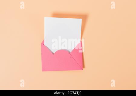 Disposizione piatta composizione minima di busta rosa con cartoncino bianco su sfondo beige. Foto Stock