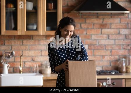 Donna felice che disimballo scatola di cartone in cucina Foto Stock