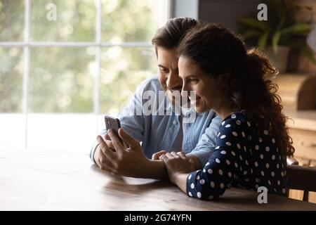 Felice giovane coppia che condivide il telefono cellulare, guardando i contenuti Foto Stock