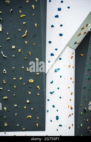 Parete artificiale per arrampicata su roccia che mostra varie impugnature colorate presso il parco avventura palestra all'aperto. Foto Stock