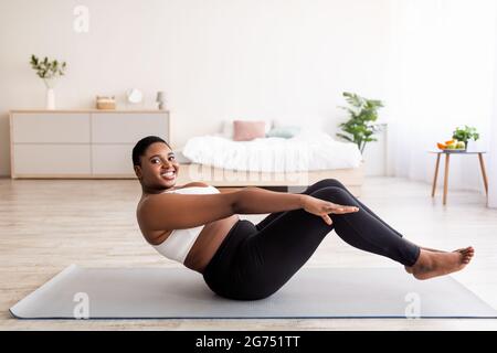 Overweight millennial nero signora fare esercizi abs, allenamento muscoli core a casa, copia spazio Foto Stock